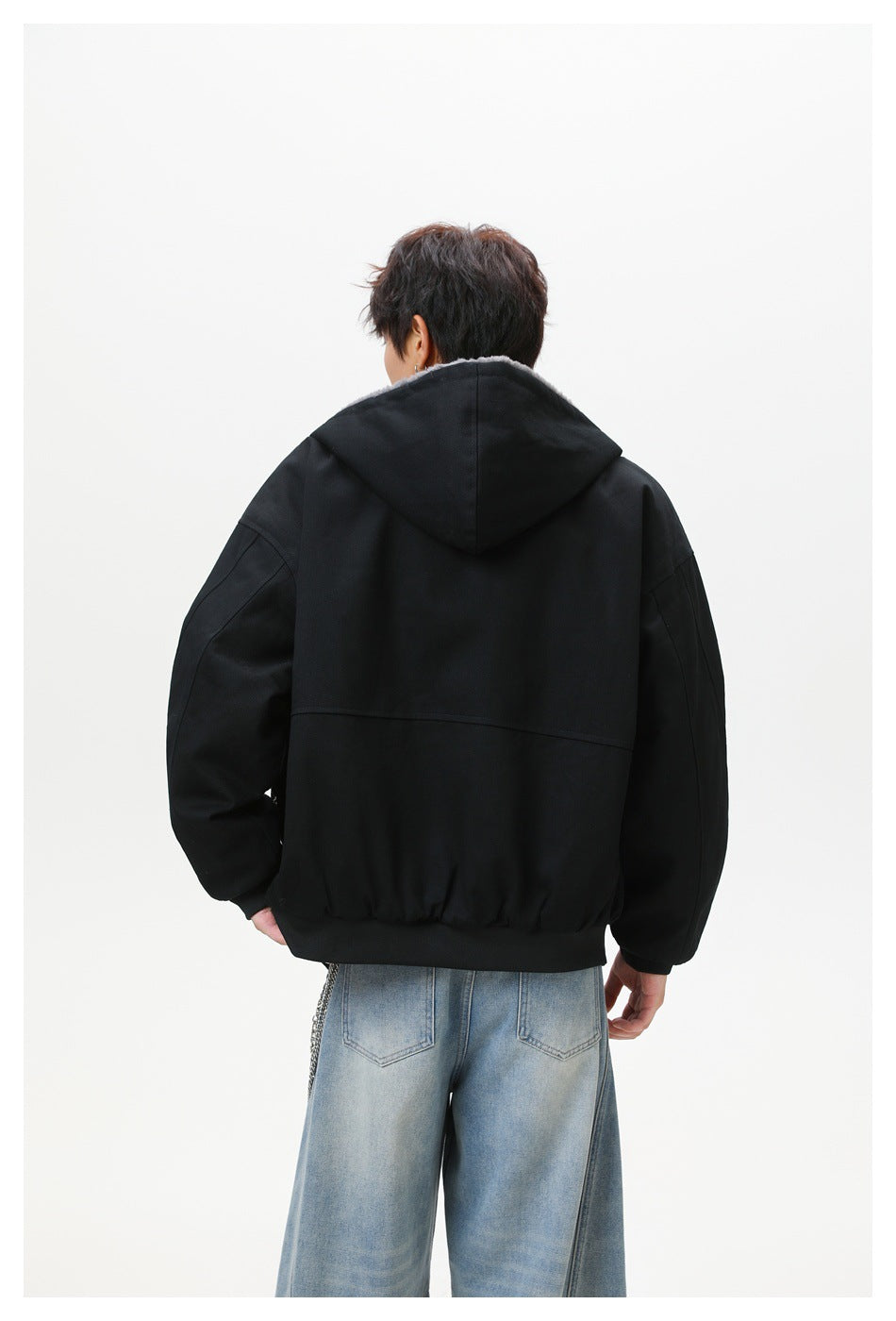 Back view of model wearing a black hooded jacket with back yoke seam and ribbed hem, with light-wash jeans