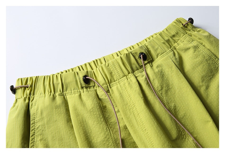 Close-up of yellow-green pants showing the gathered waistband and multicolored drawcords with black toggles.
