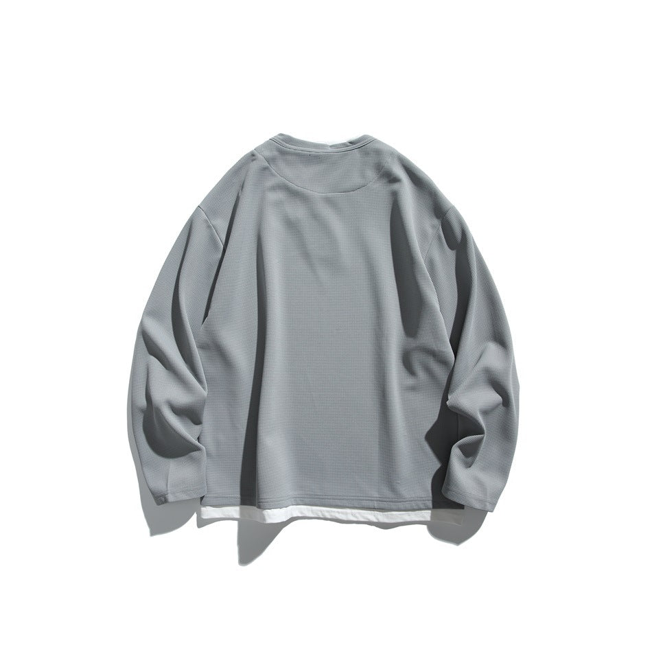Back view of a gray long-sleeve textured top layered over a white shirt, laid flat on a white background.