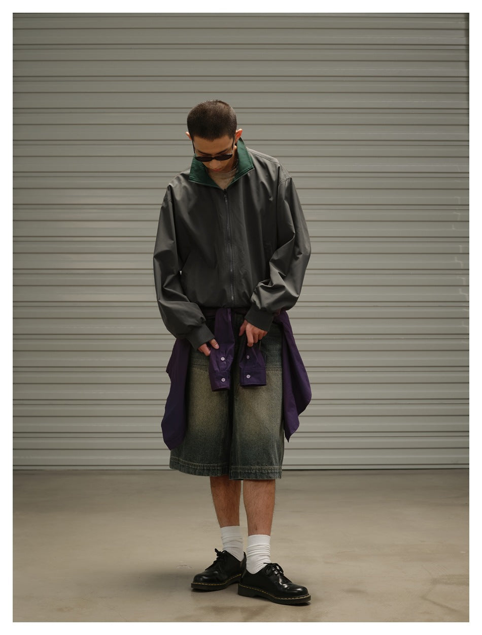 Model wearing a charcoal zip jacket with a dark green collar and a purple jacket tied over faded denim shorts.