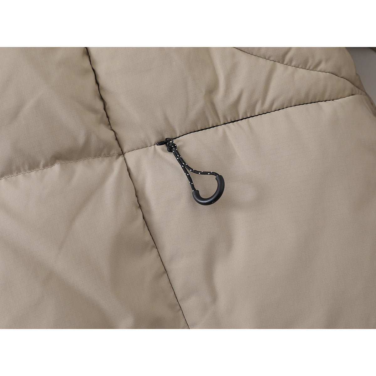 Close-up of a black drawcord toggle on the beige jacket's quilted fabric.