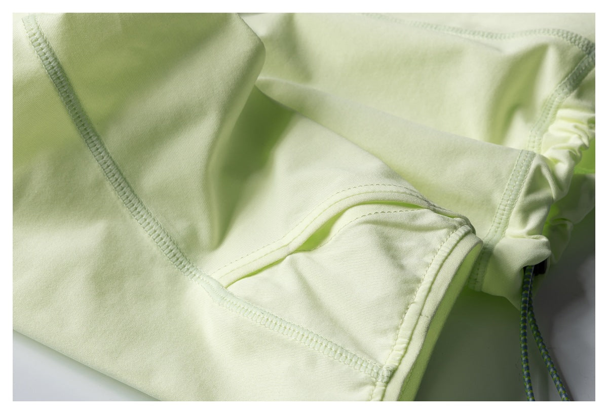 Close-up of pale lime garment seams with a narrow drawcord visible at the edge.