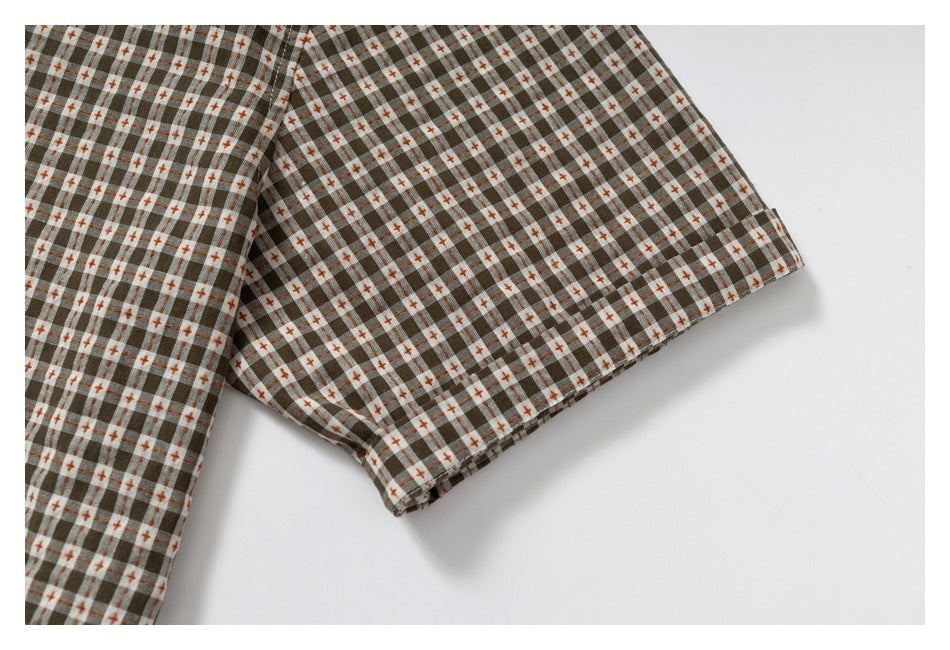 Close-up of the short sleeve and hem of a brown, gray, and cream checked shirt with orange accents.