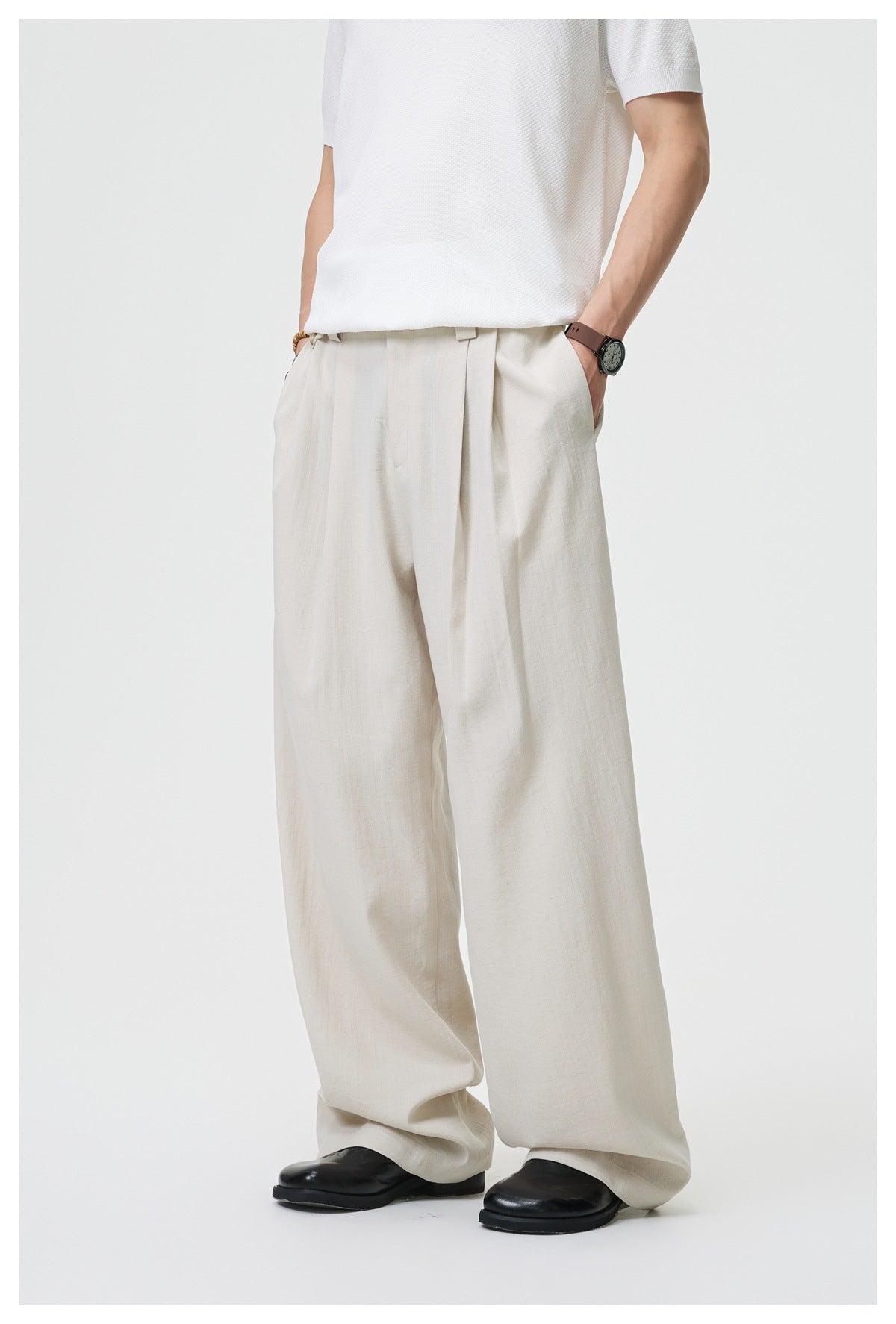 Close front view of loose ivory trousers worn with a white top, showing the waistband, pleats, and wide legs.