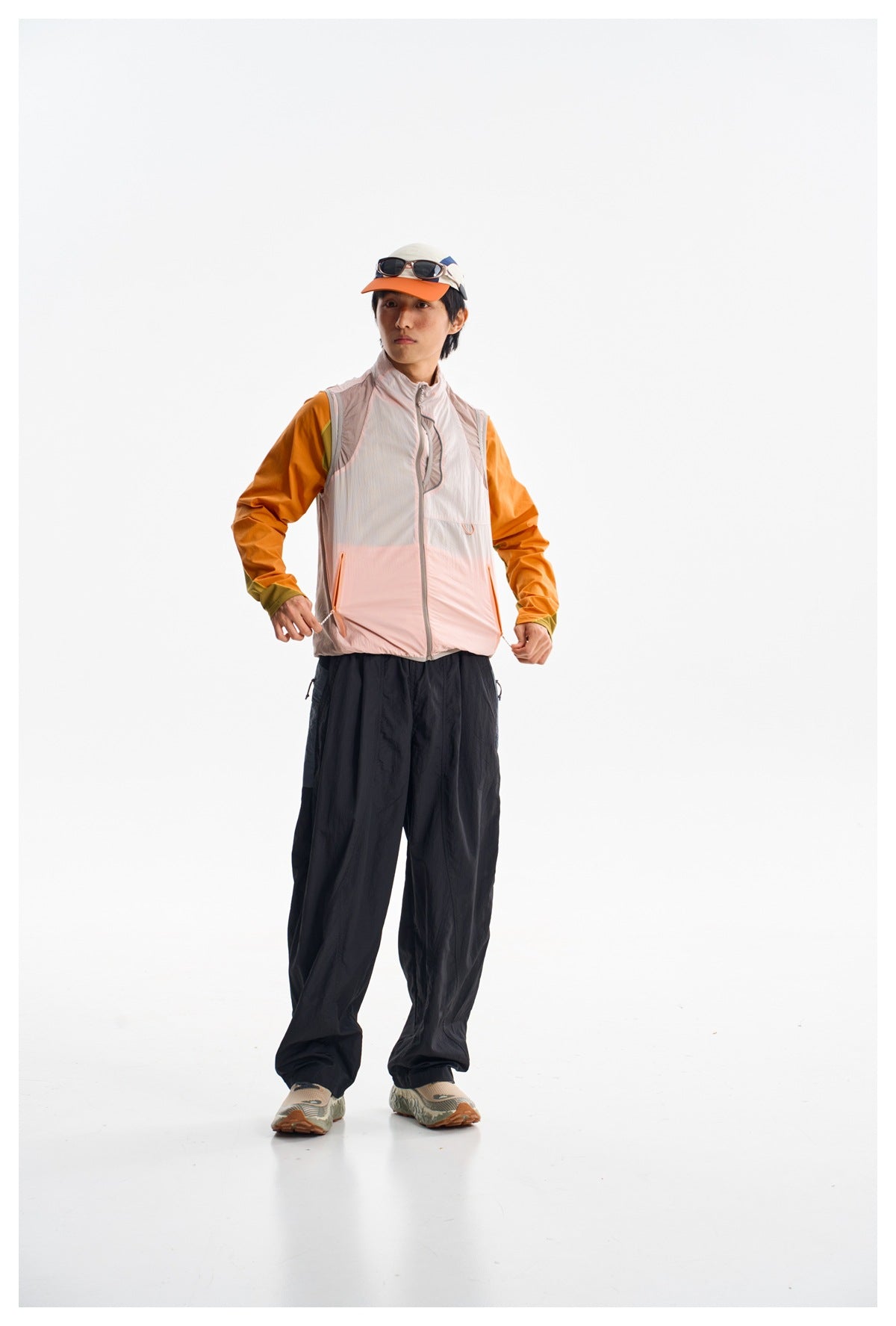 Model wearing loose black pants and a pale pink zip vest over an orange top, front view.