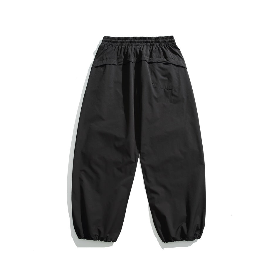Black relaxed-fit pants laid flat, showing an elastic waistband, rear pocket, and gathered ankle cuffs.