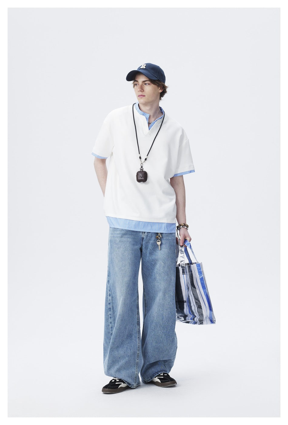 Model wearing an oversized white V-neck short-sleeve tee over a blue-and-white striped shirt with wide-leg jeans.