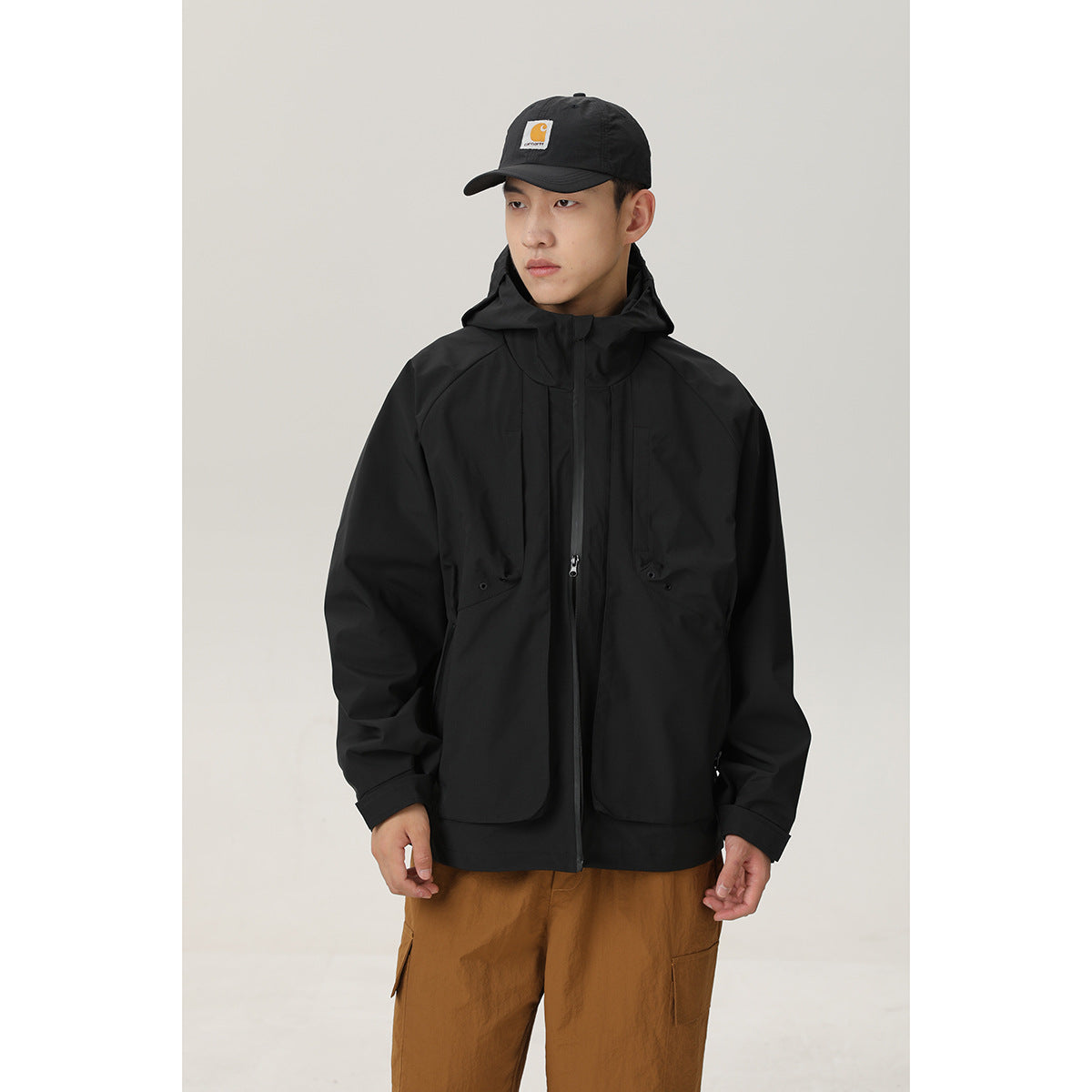 Front view of a model wearing a black hooded jacket with a zip front and flap pockets.