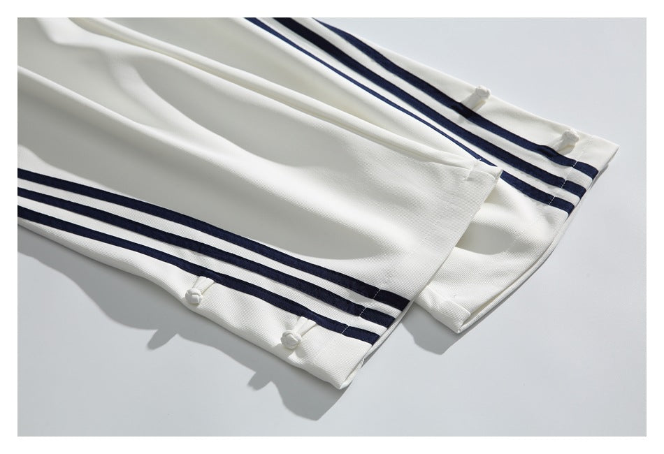 Close-up of white trouser hems with navy stripes and small knotted fasteners.
