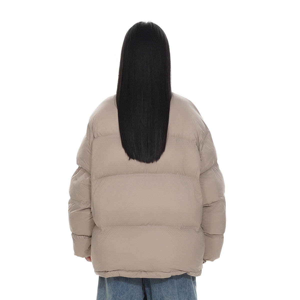 Rear view of a model wearing an oversized taupe quilted puffer jacket with blue jeans.