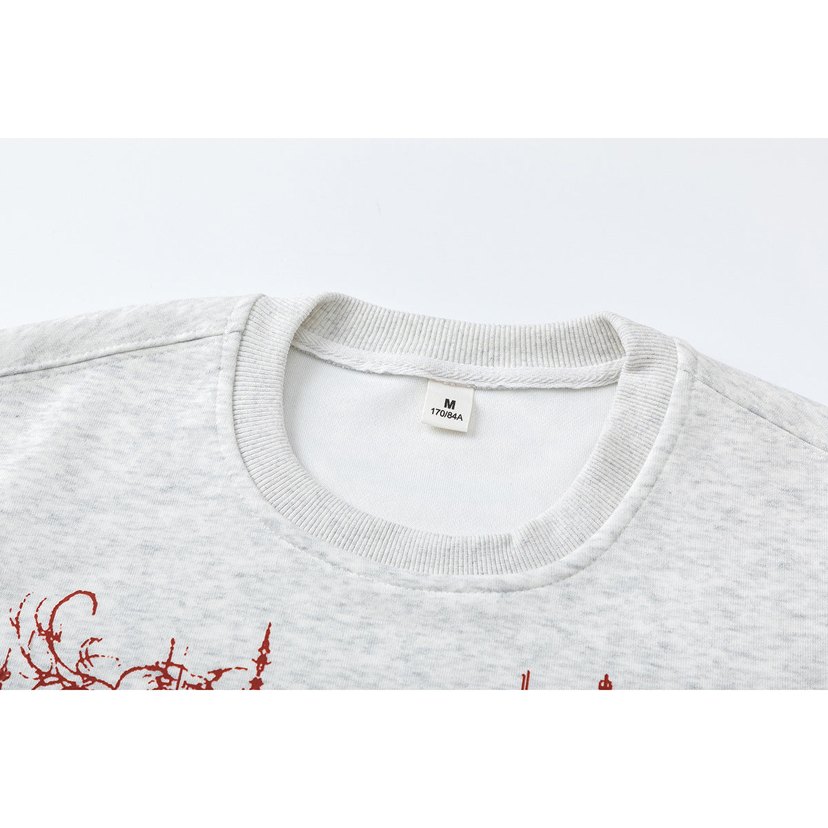 Close-up of a light heather-gray sweatshirt's ribbed crew neck and M size label; red print is partly visible below.