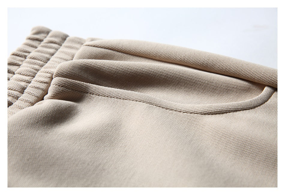 Close-up of a curved side pocket on beige shorts, with the elastic waistband visible.