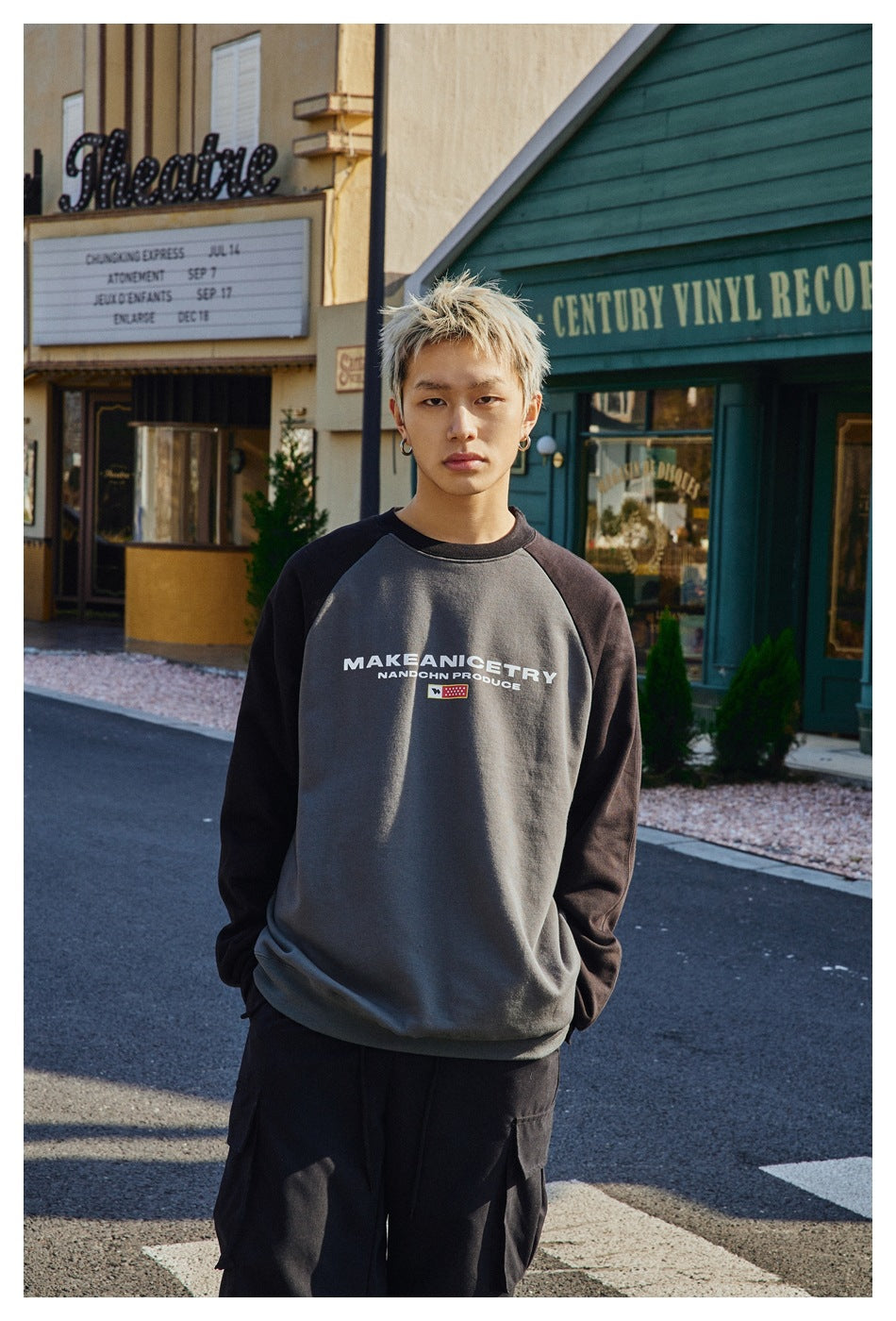 Close-up of a model wearing a gray crewneck sweatshirt with black raglan sleeves and chest print, hands in pockets
