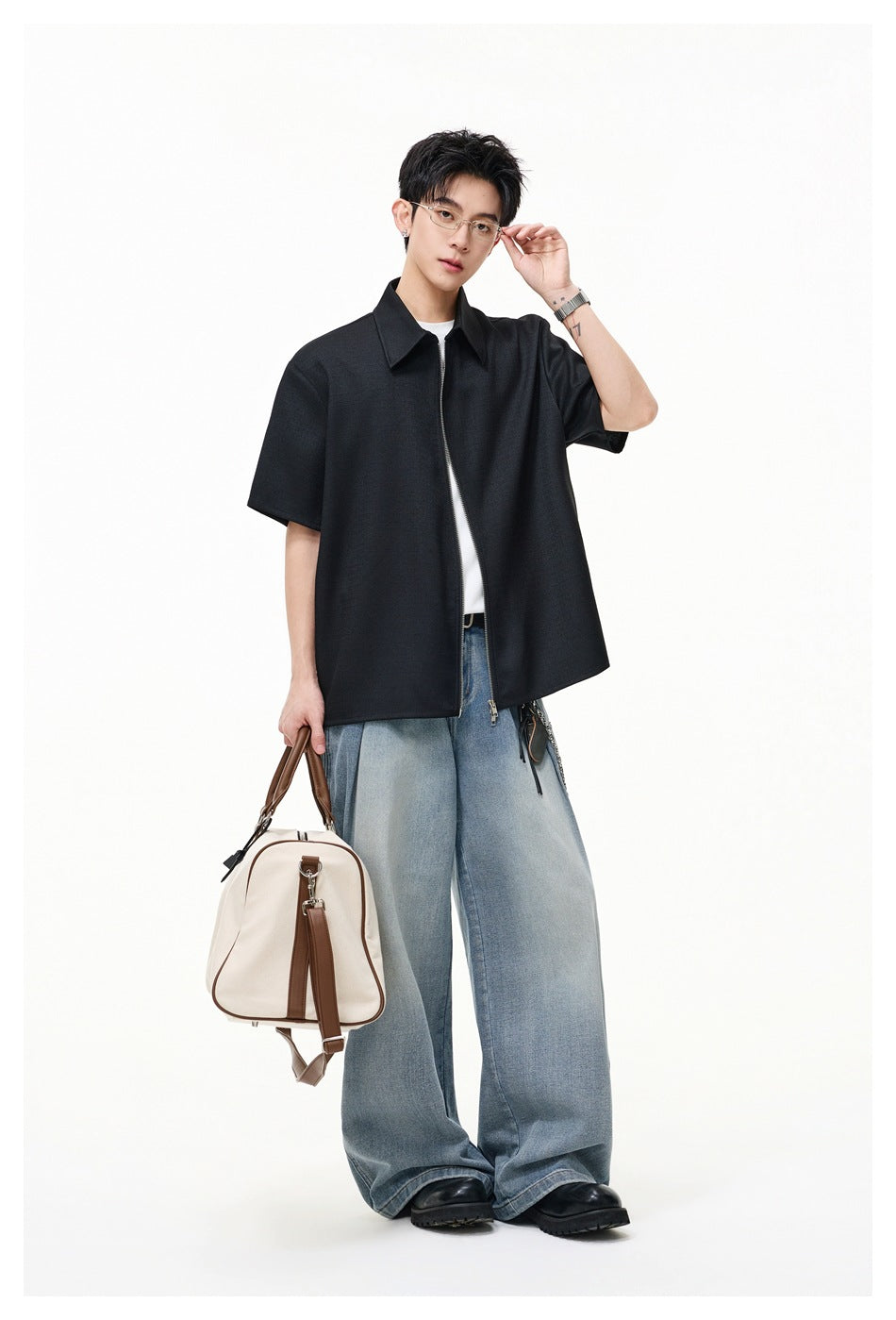 Full-length model wearing a black short-sleeve collared zip-front shirt and wide-leg blue jeans.