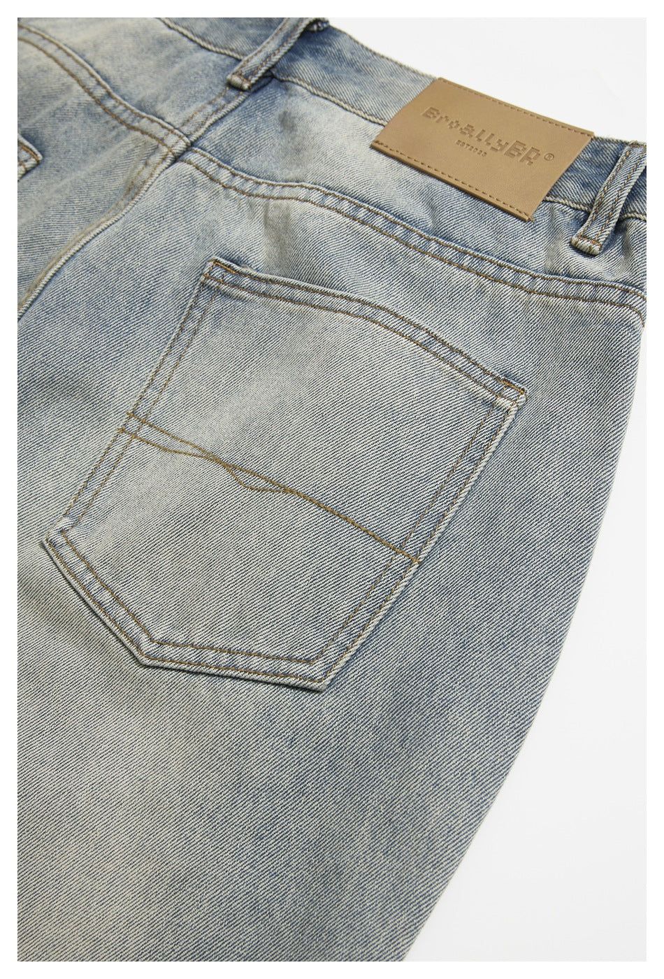 Close-up of a back pocket and belt loops on light-wash blue jeans, with a tan embossed leather waistband patch.