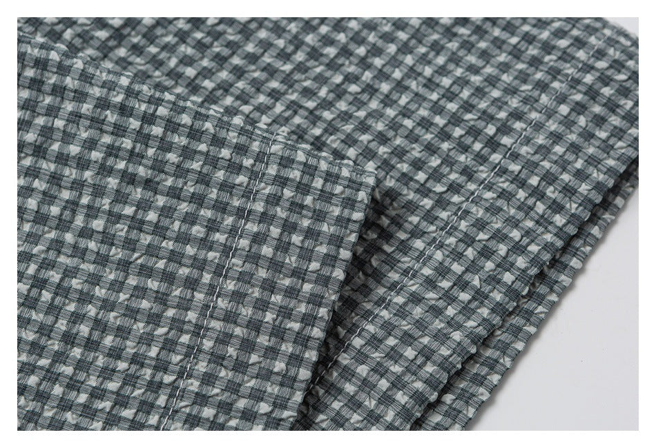 Close-up of overlapping gray check shirt fabric, showing a folded edge and stitching.
