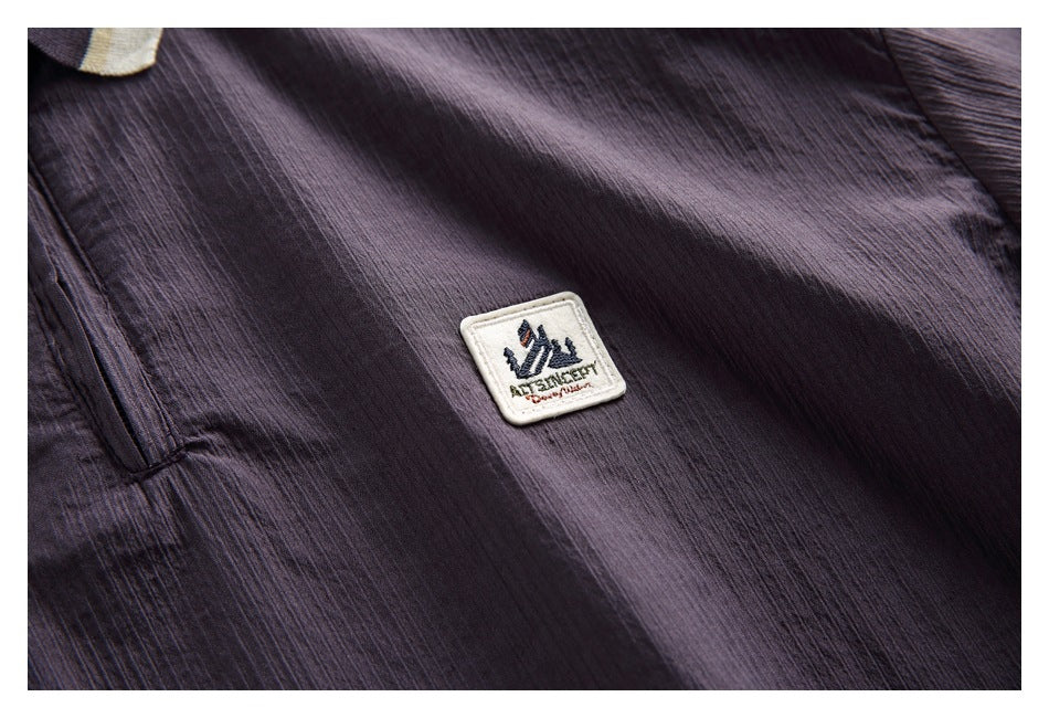 Close-up of a dark plum garment with a small cream embroidered mountain-logo patch.