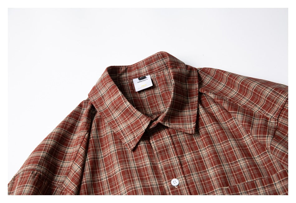 Close-up of a rust-red plaid short-sleeve shirt showing its collar, front placket, and chest pocket.
