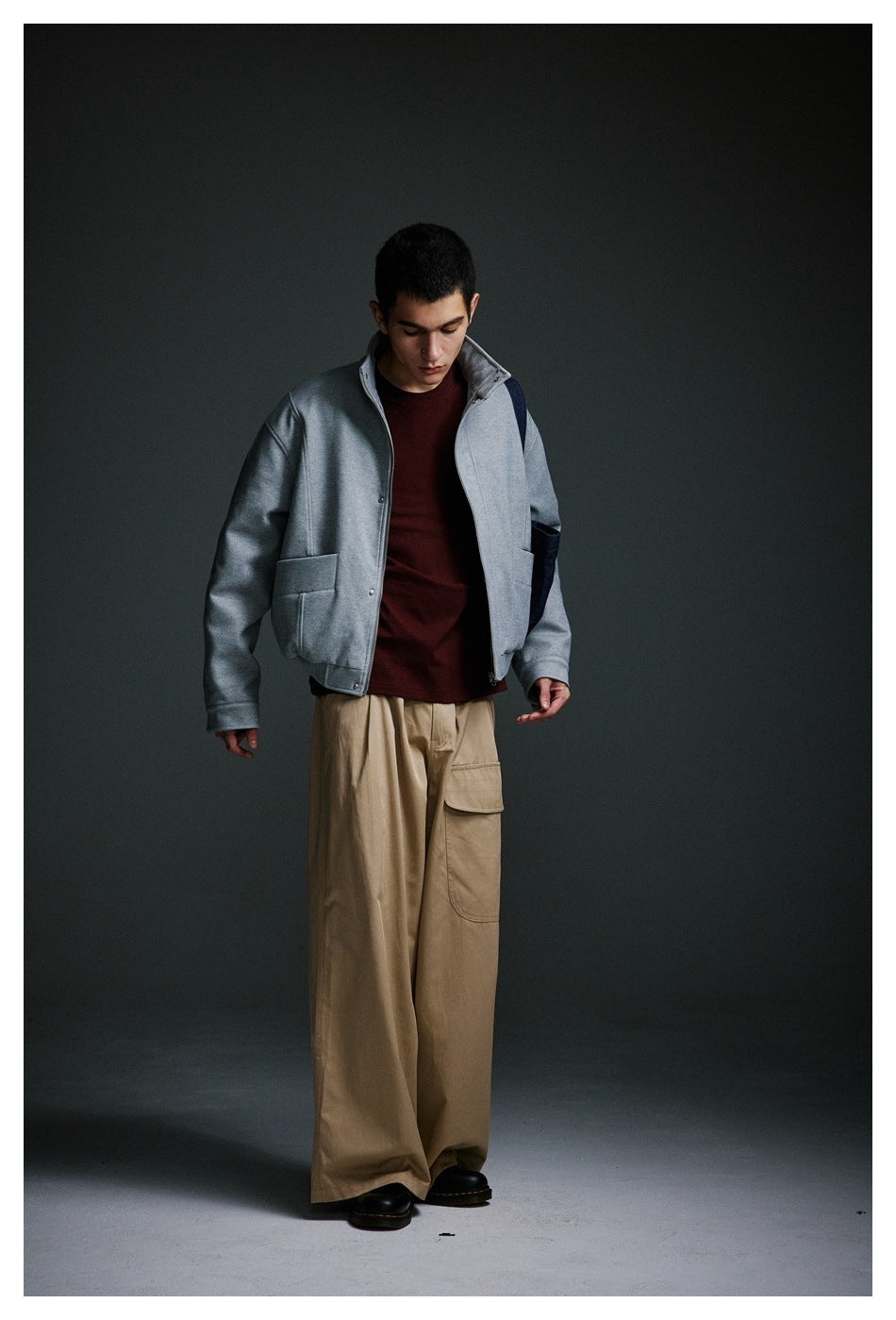 Model wearing a light gray jacket with dark navy panels over a burgundy top and wide tan cargo trousers.