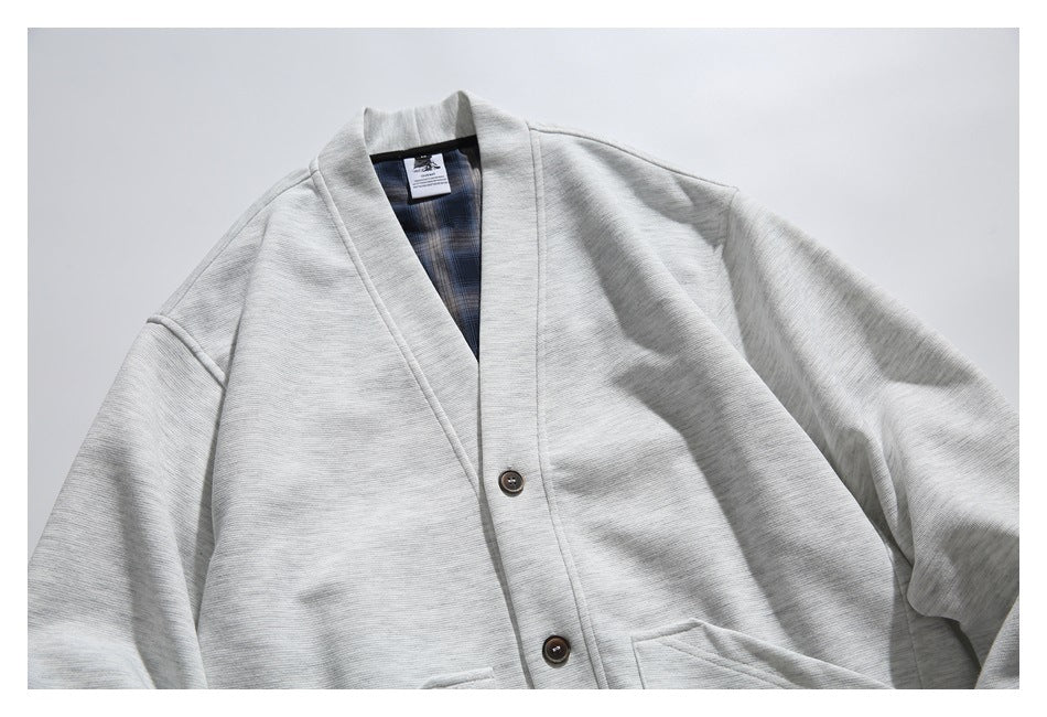 Light gray shawl-collar cardigan laid flat, showing its blue plaid inner facing and dark front buttons.