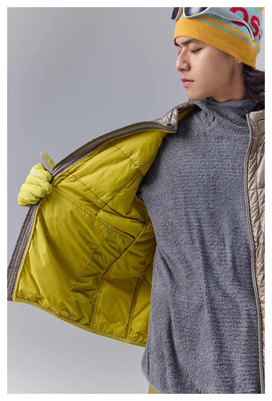 Close-up of a taupe jacket opened to show its bright yellow quilted lining and a gray fleece top.