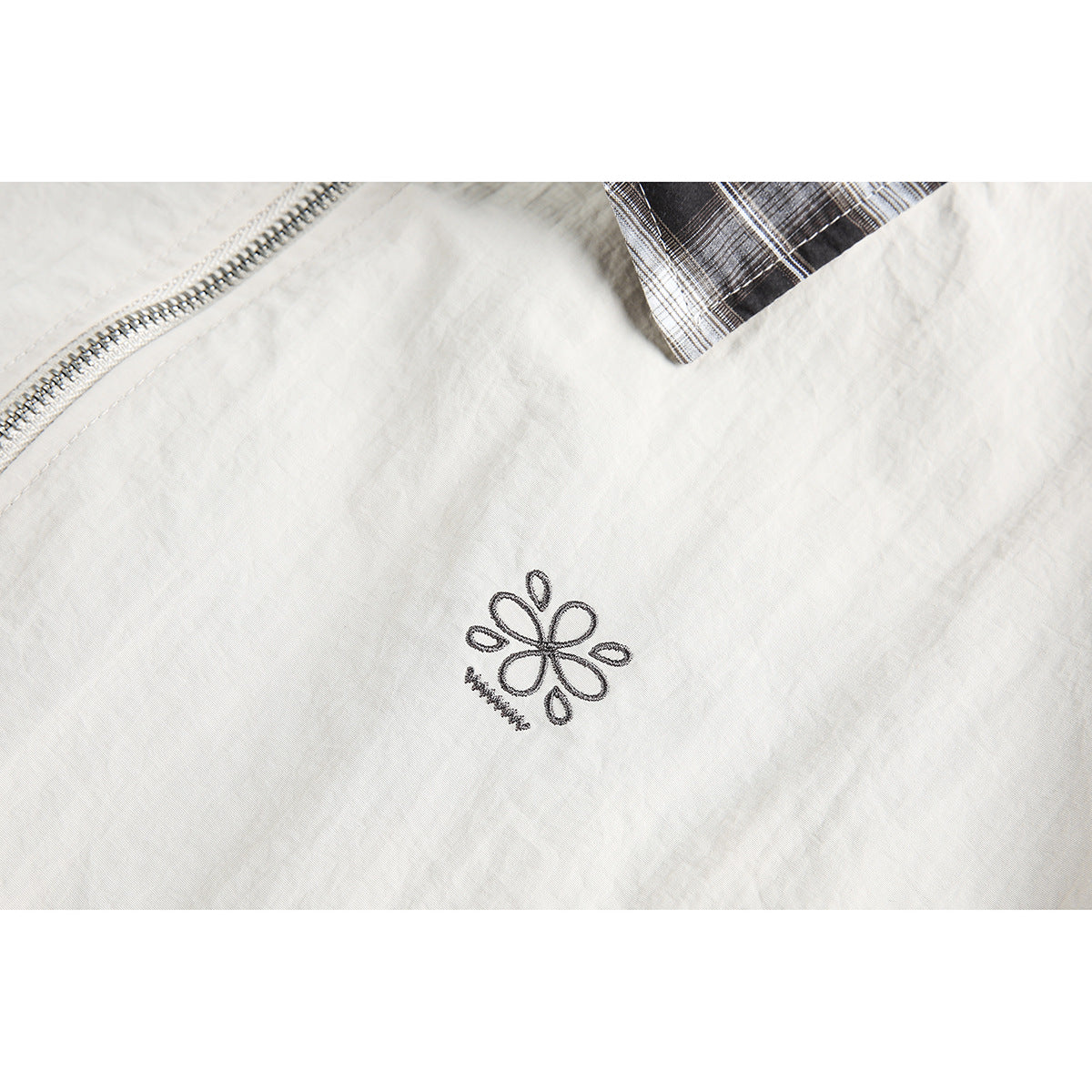 Close-up of a small embroidered floral motif on the cream jacket fabric, beside the zipper and plaid trim.
