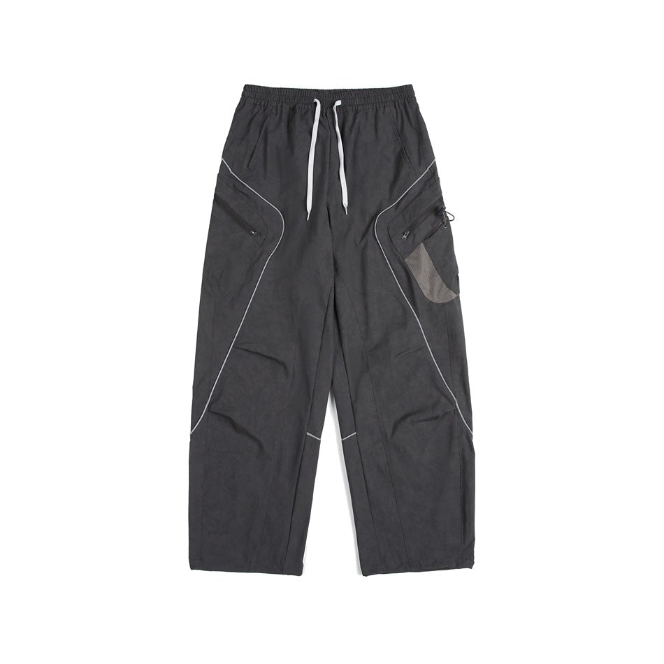 Front view of loose charcoal cargo pants with an elastic waist, white drawstrings, curved piping and zip pockets.