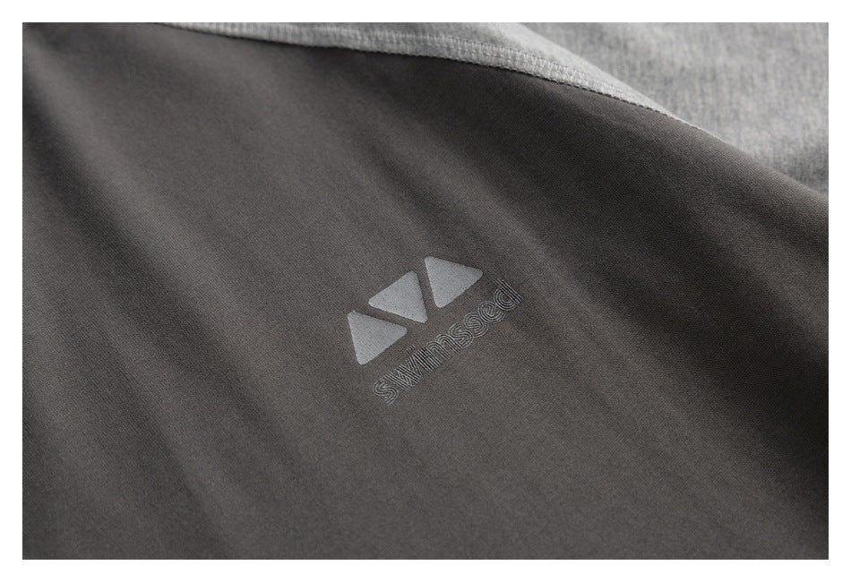 Close-up of a dark charcoal garment with a small light-gray geometric logo and lettering printed on the fabric.