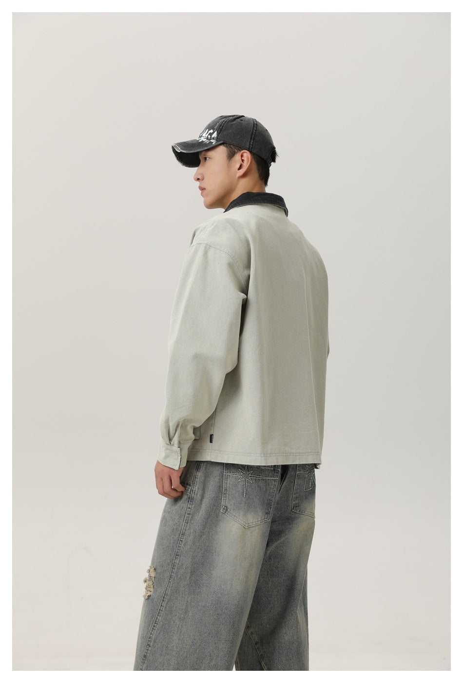 Rear three-quarter view of a model wearing a pale sage jacket with a black collar and a plain back.