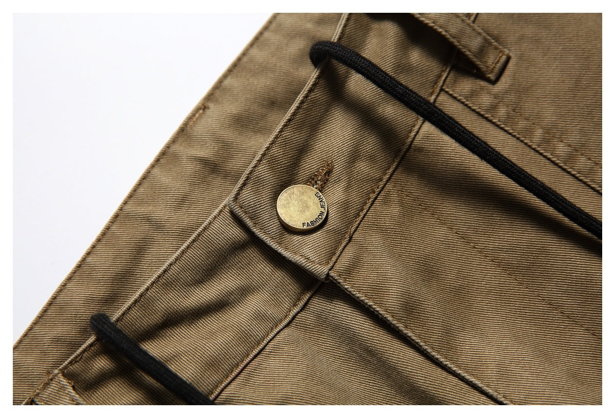 Close-up of a brass button, belt loop and black drawstring on tan-brown trousers.