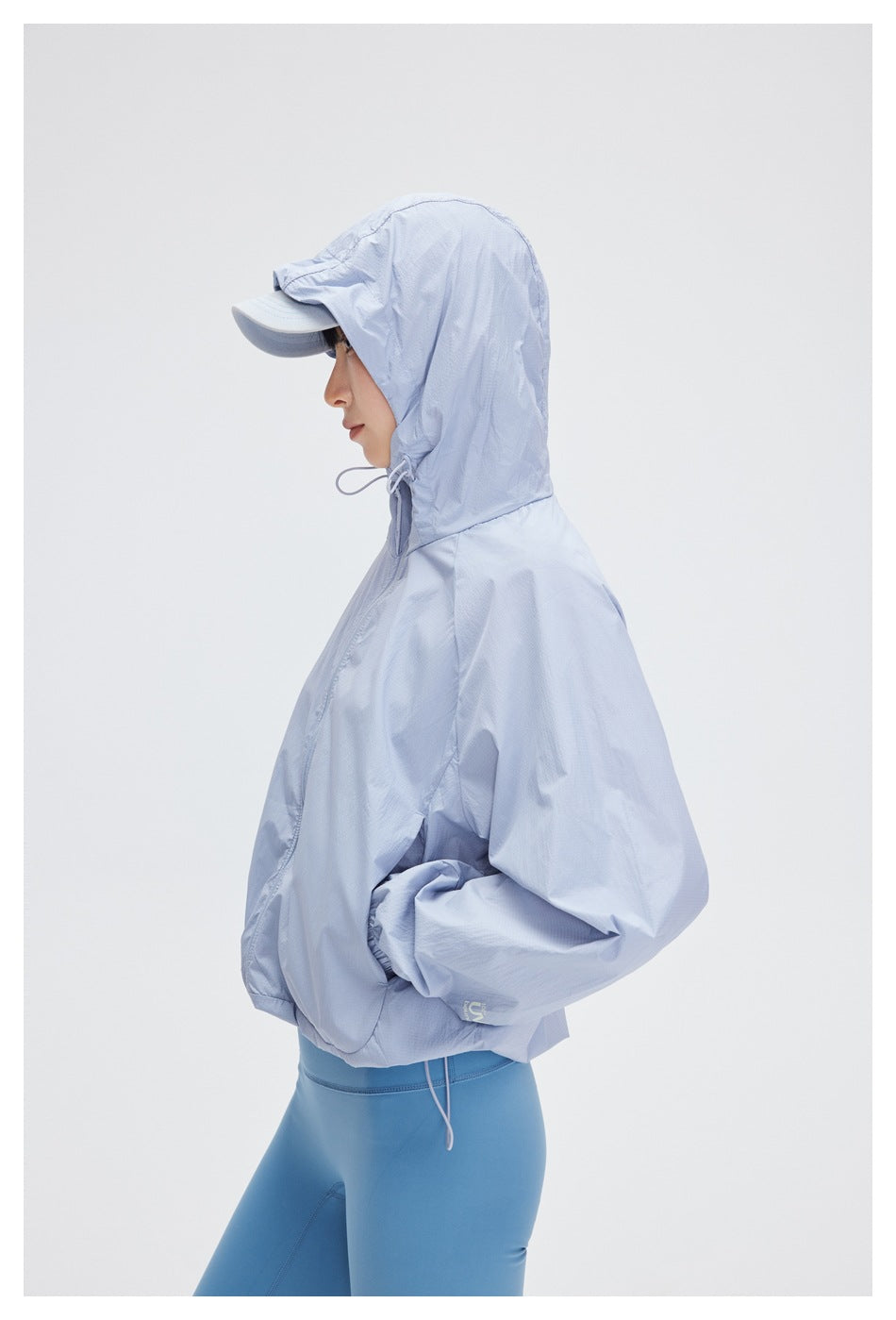 Side view of a woman wearing the pale blue jacket with its hood up over her cap.