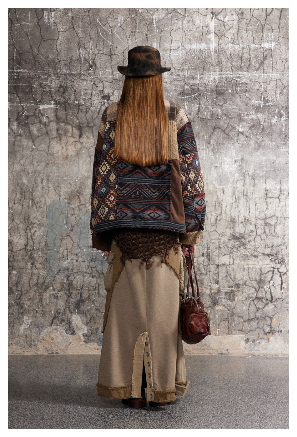 Back view of a model wearing the patchwork jacket with plaid yoke and geometric panel, hat, long skirt and bag