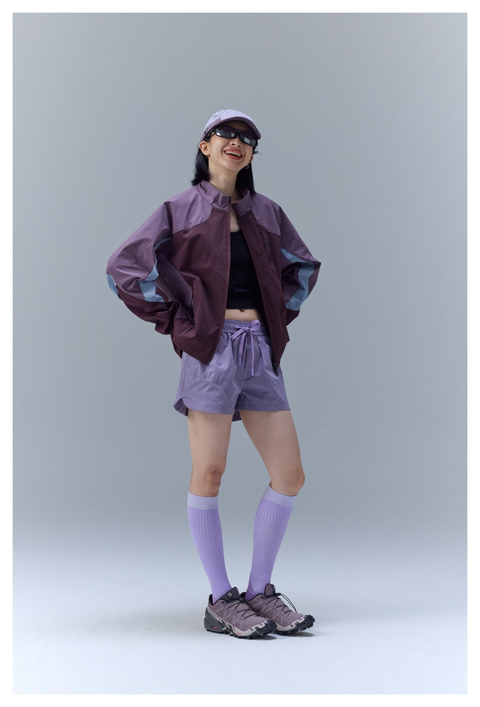 Woman posing in a burgundy and lavender color-block jacket with pale sleeve stripes and matching lavender shorts.