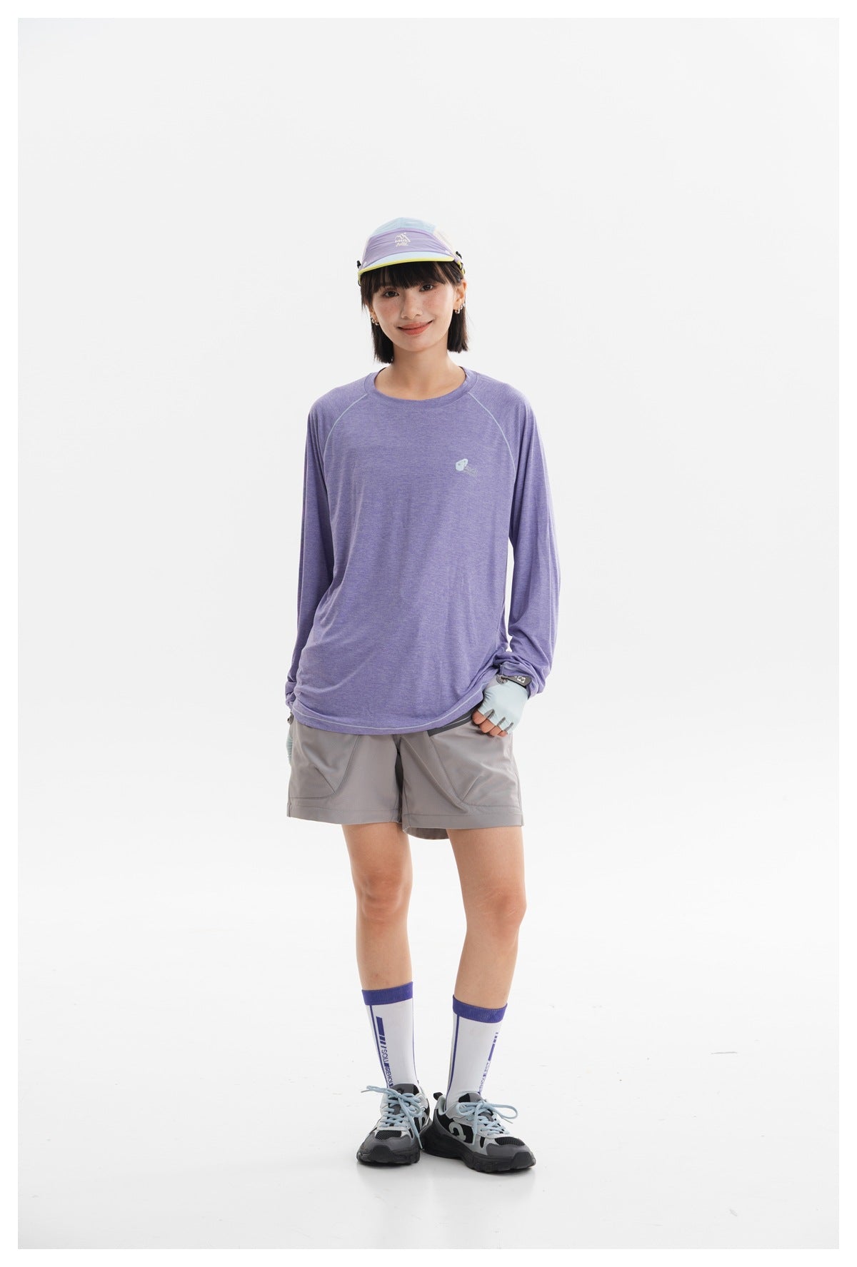 Front view of a model in a lavender long-sleeve top and gray outdoor shorts, with a visor, gloves, and hiking shoes.
