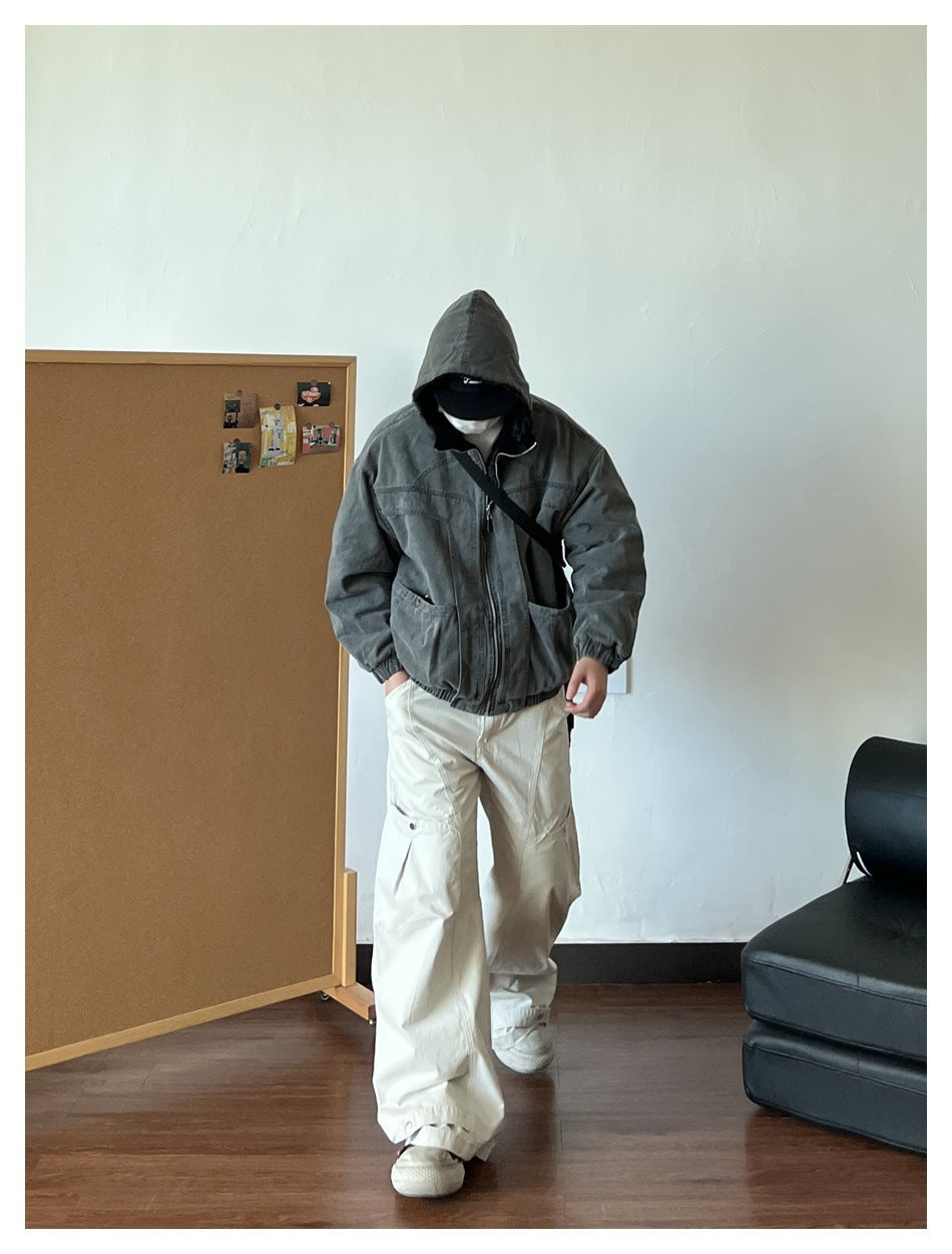 Person wearing a dark charcoal hooded zip jacket with large front pockets, shown with loose cream cargo pants.