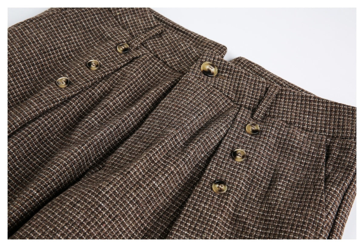Close view of the front waist and pleats of brown small-check trousers, with several brass-tone buttons.