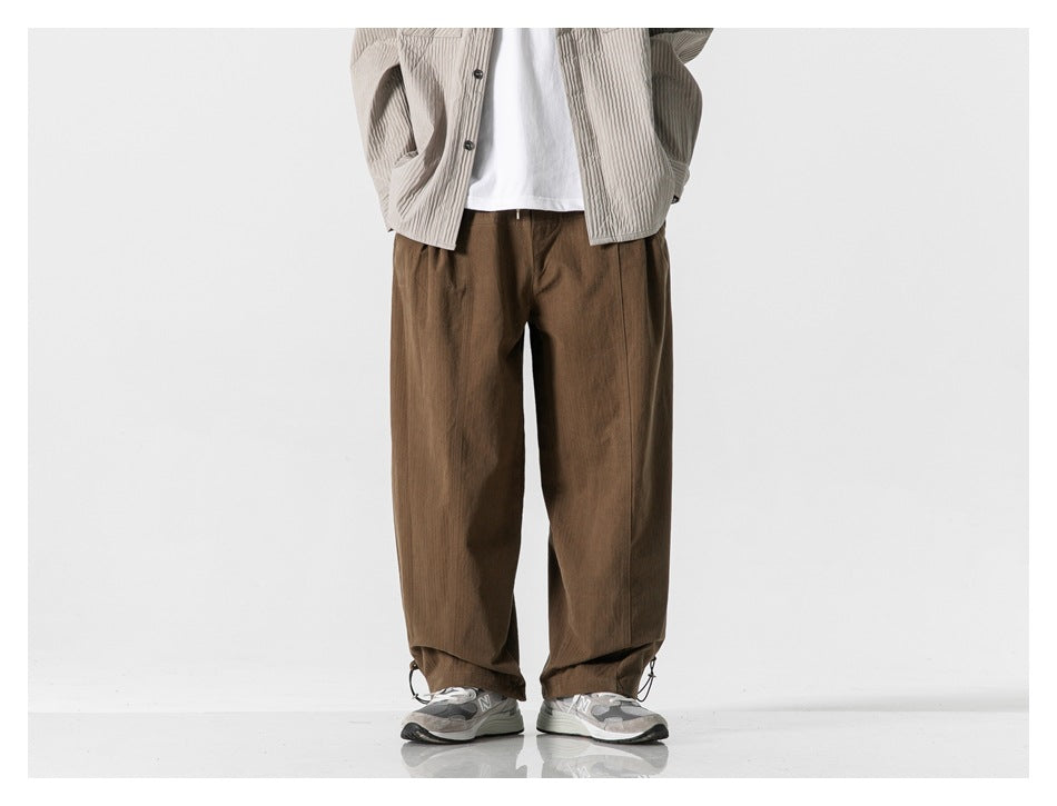 Front view of a model wearing relaxed brown trousers with adjustable drawcord hems.