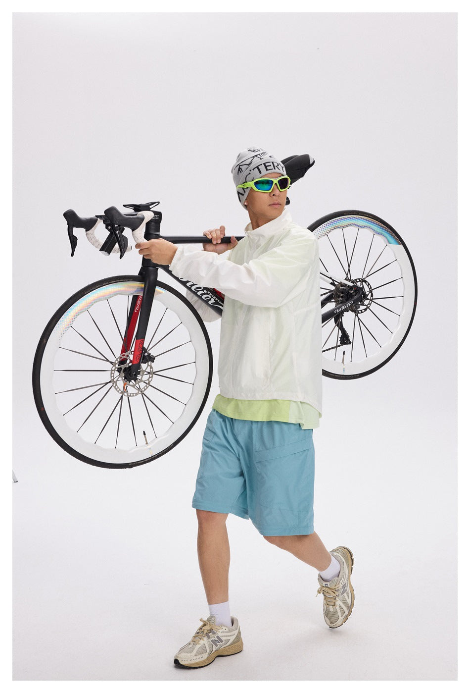 A man in a pale jacket and blue shorts carries a road bike over his shoulder.