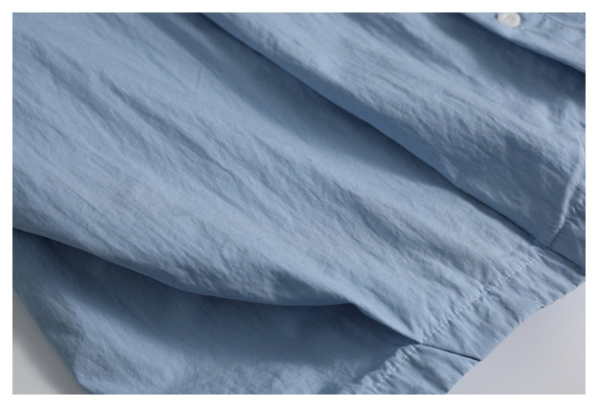 Close-up of the light blue shirt's stitched lower hem and softly folded fabric.