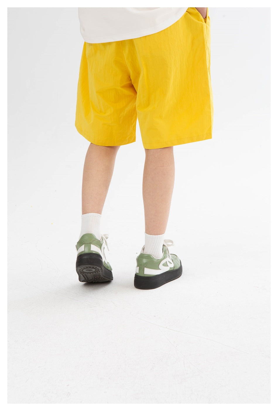 Rear view of a model wearing bright yellow knee-length shorts, showing the plain back and green sneakers.