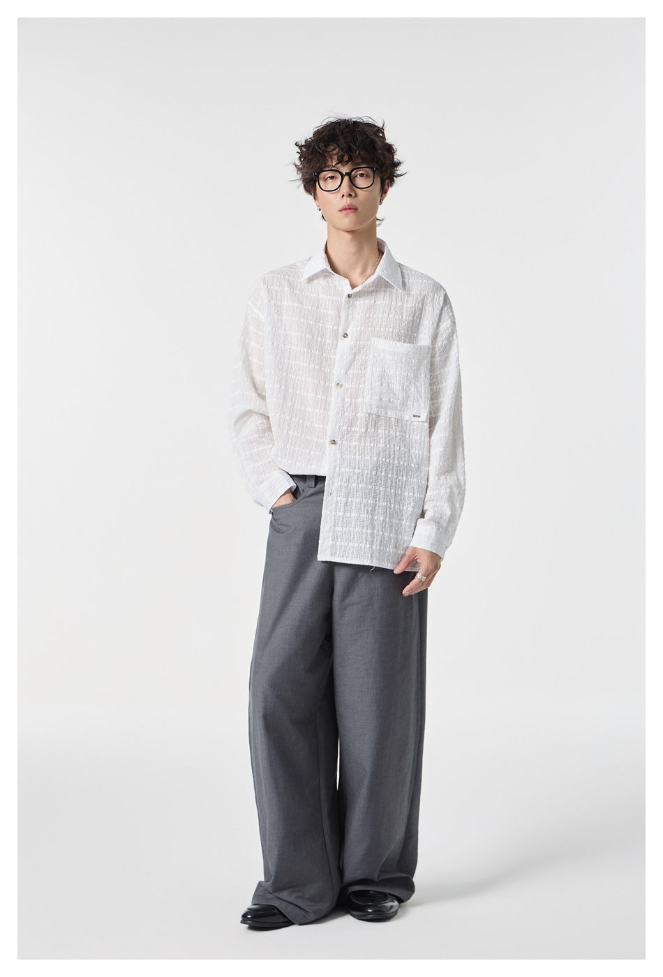 Standing model wearing a white textured button-up shirt with a chest pocket and gray wide-leg trousers.