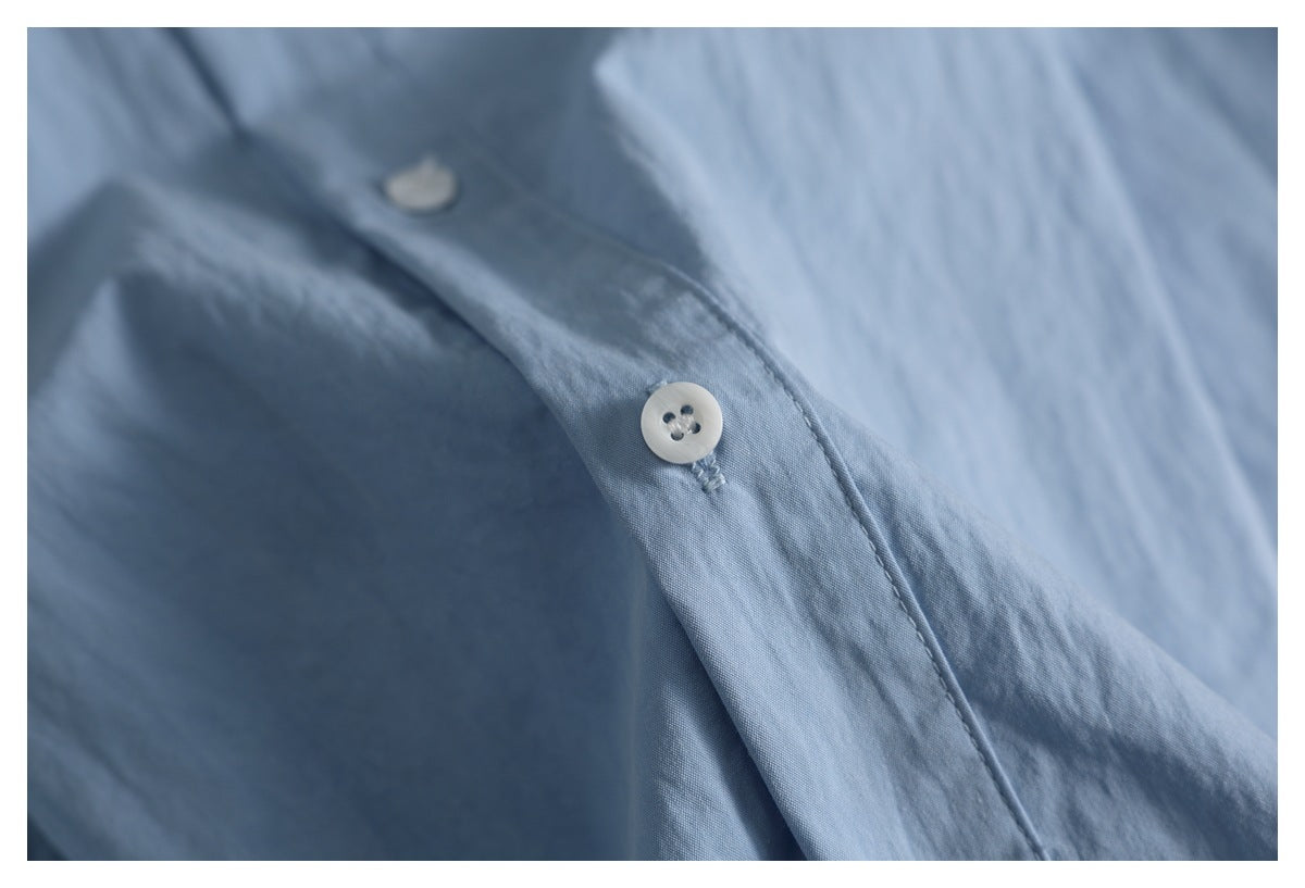 Close-up of a white four-hole button and stitched placket on a light blue shirt.