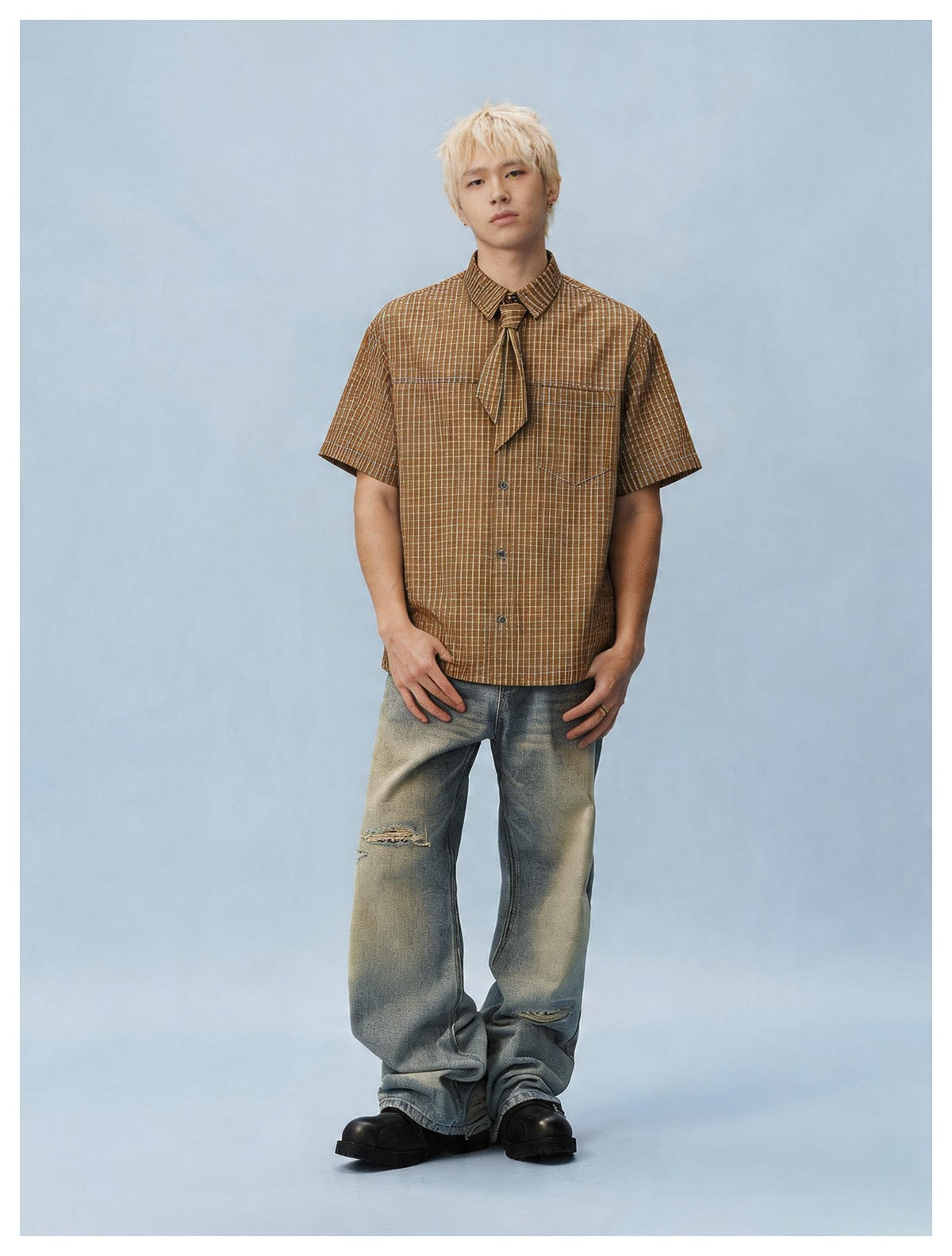 Model wearing mustard yellow plaid short-sleeve shirt with neck tie, faded distressed jeans and black boots