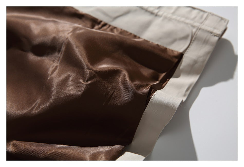 Close-up of glossy brown garment fabric beside a light beige stitched edge and seam.