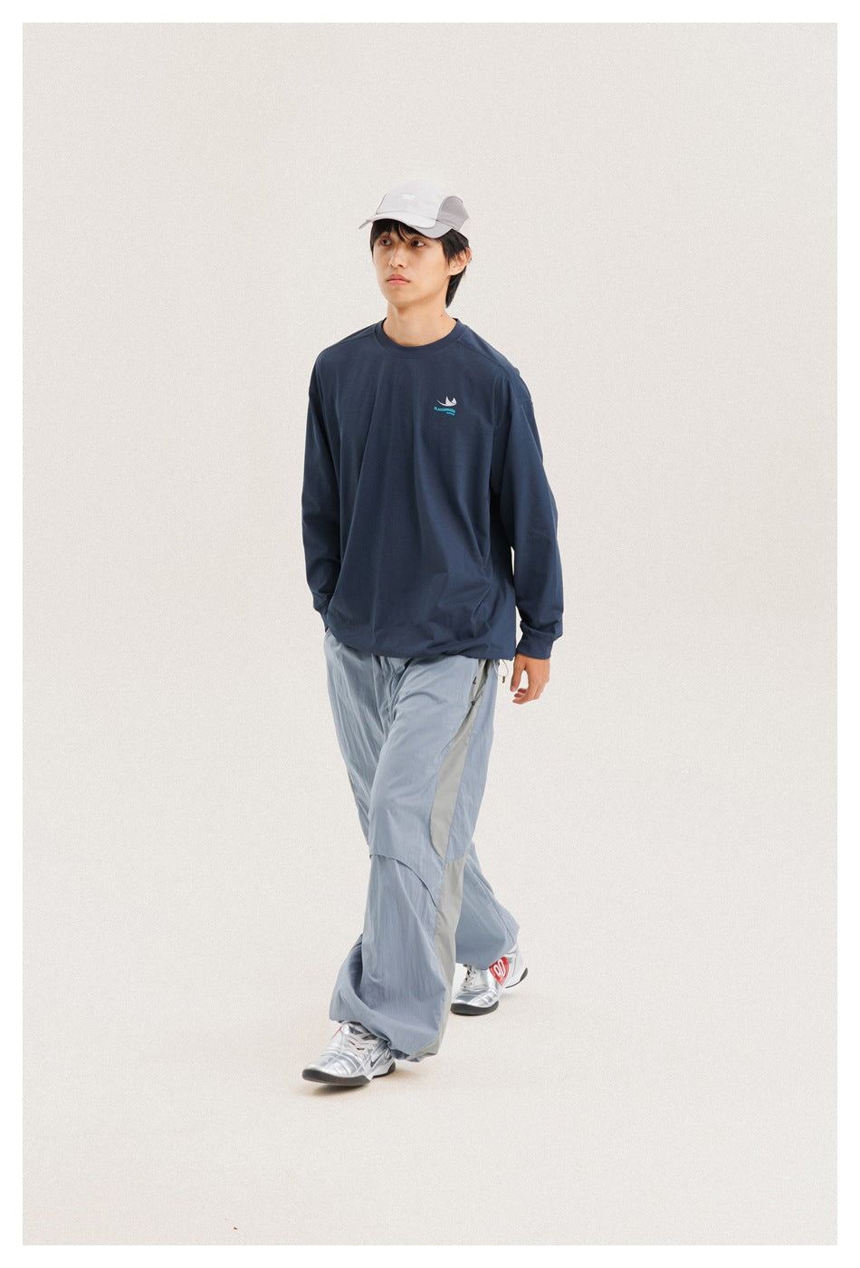 Full-length view of a model walking in a navy long-sleeve shirt, pale blue wide-leg pants, and a light cap.