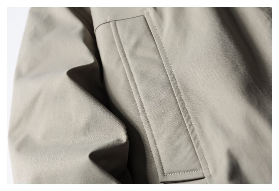 Close-up of a taupe garment's rectangular welt pocket and stitching.
