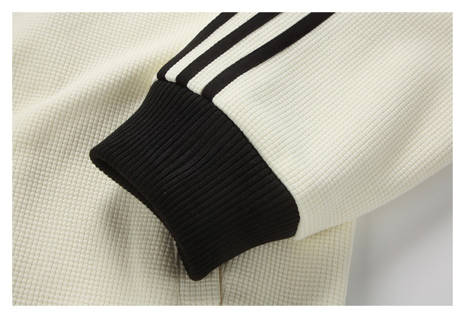 Close-up of a black ribbed cuff and three black stripes on a cream sleeve.