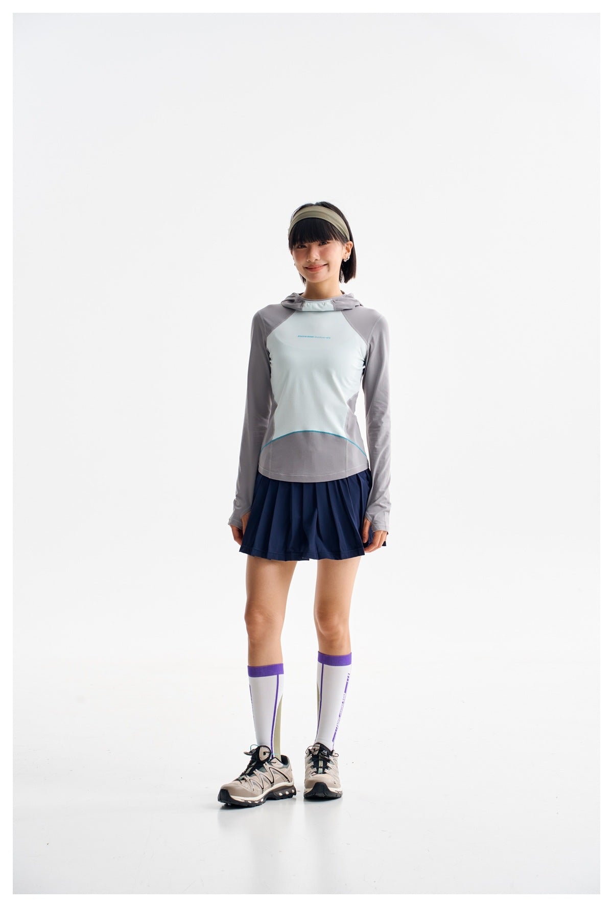 Model wearing gray and pale mint color-block hooded long-sleeve top with navy pleated skirt and tall socks