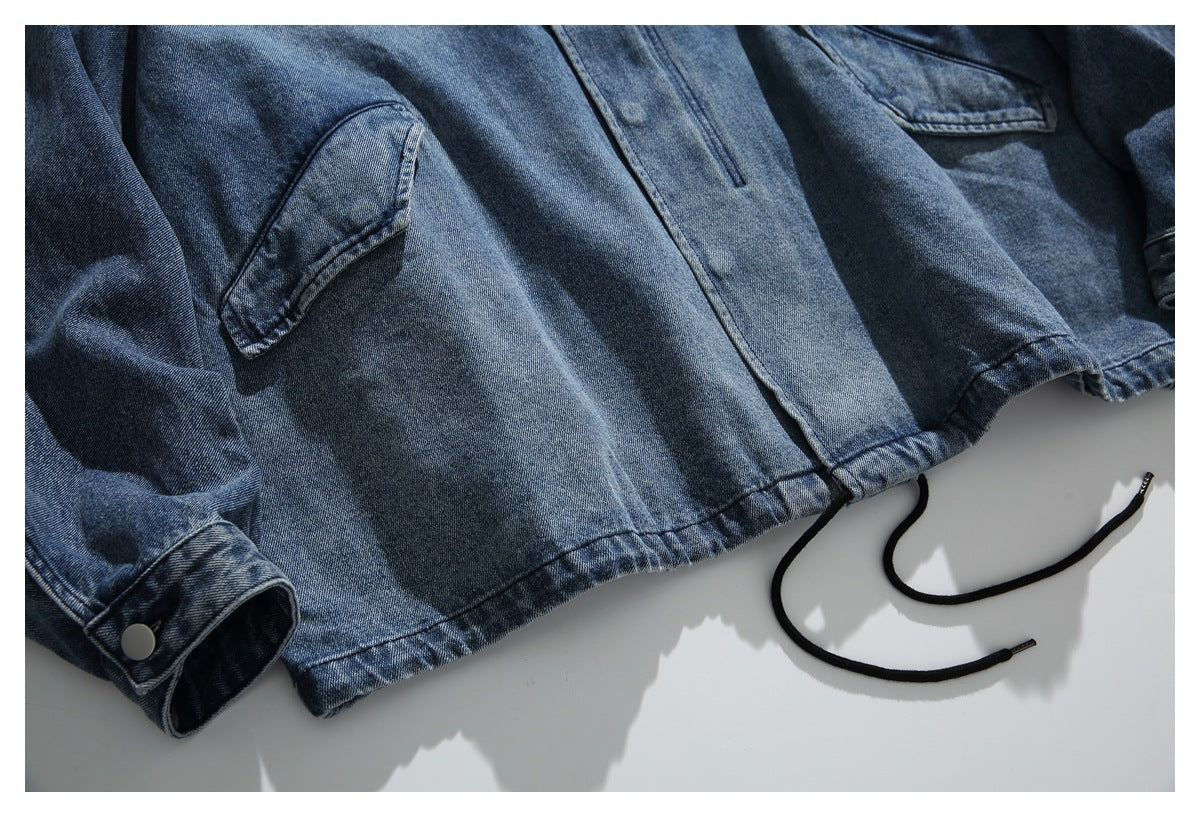 Close-up of a blue denim jacket hem, snap-button cuff, and black drawstrings.