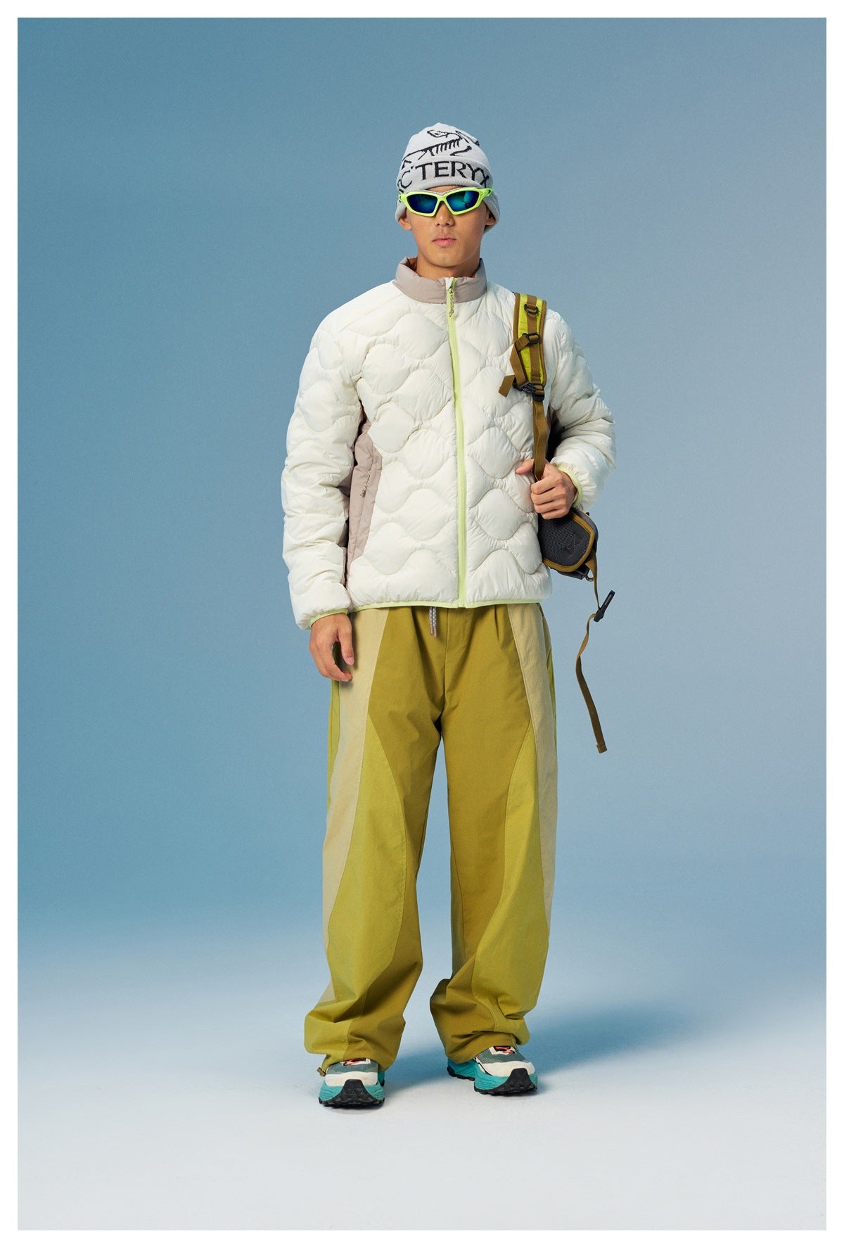 Model wears an ivory wave-quilted jacket with a lime zipper and taupe collar, paired with olive trousers.